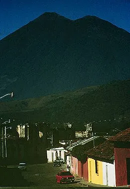 Town street with colorful buildings with a large volcano in the background at night