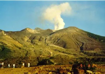 Green covered volcanic mountain range with a plume of smoke rising into the sky