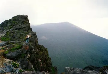 A man stands confidently at the mountain's edge, overlooking a breathtaking landscape below. 