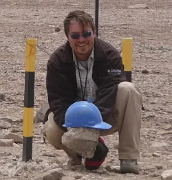 Dr. Axel K. Schmitt crouching and holding a rock smiling